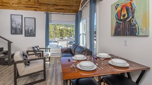 Un coin repas avec une table en bois dressée pour quatre personnes, un canapé en cuir et un grand tableau représentant un ours accroché au mur.