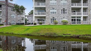 A multi-story stone building with balconies, a grassy lawn, and a pond. - Breathe deep | swing free | rest in comfort | Magnolia Place 4789-104 (Myrtle Beach)