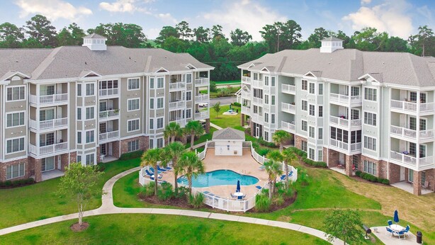 A multi-story residential building with a central courtyard featuring a swimming pool, surrounded by lush greenery and palm trees. - Inviting 3-Bed Magnolia Pointe Condo Retreat | Magnolia Pointe Luster Leaf 4894-301 (Myrtle Beach)