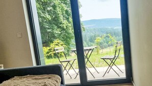 Una habitación con un gran ventanal corredero que da a un patio exterior con mobiliario de madera.