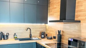 Una cocina moderna con armarios oscuros, encimera de madera, horno empotrado y microondas.