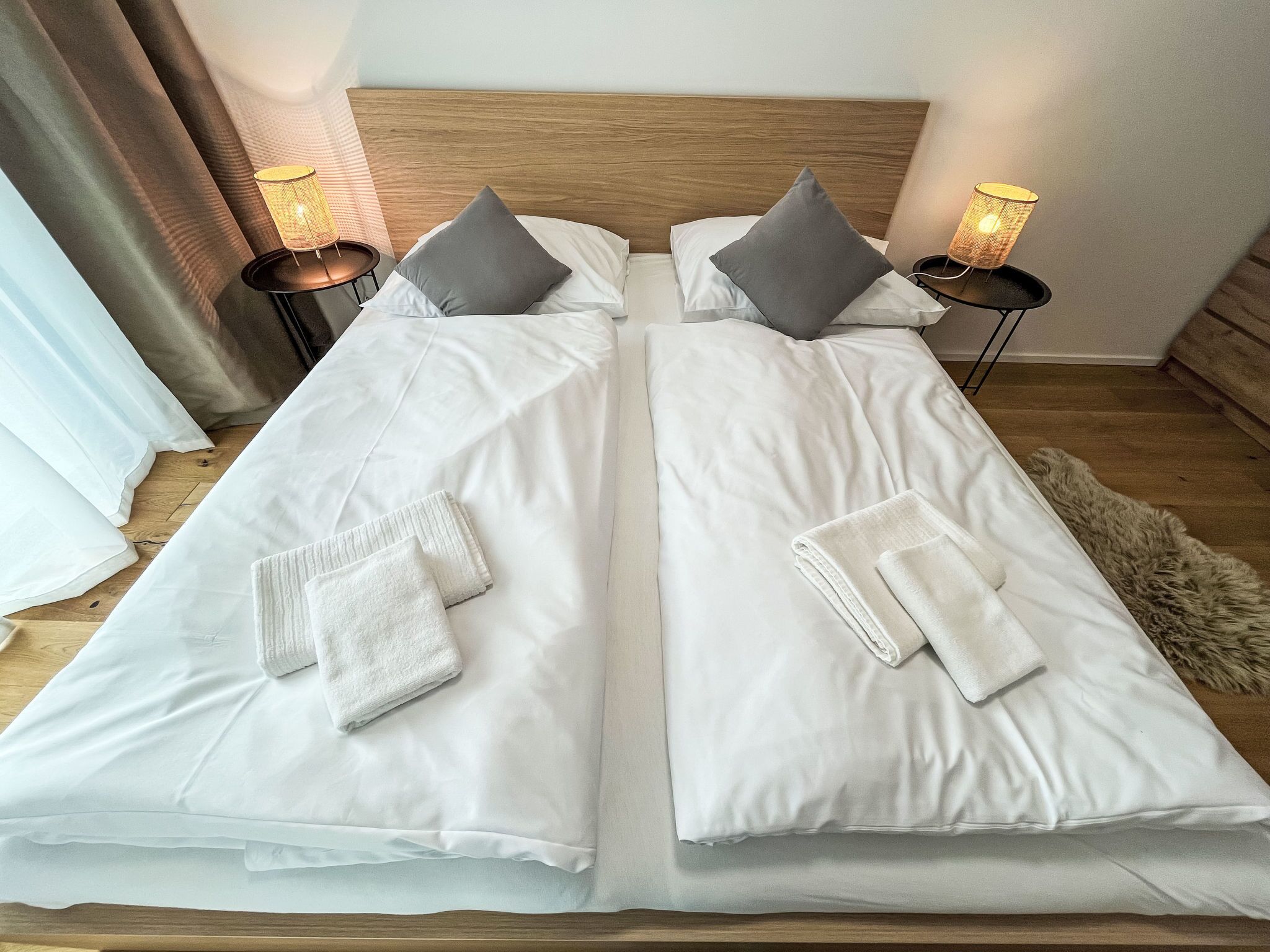 Een tweepersoonsbed met witte lakens, twee kussens en twee bedlampjes.