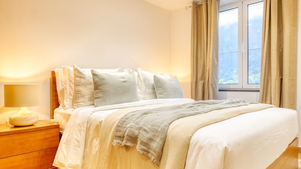 Un dormitorio con cama, mesita de noche y ventana con cortinas.