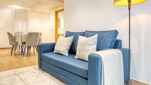 Una sala de estar moderna con un sofá azul, una mesa de comedor con sillas y una lámpara de pie.