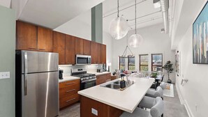 Una cocina moderna con electrodomésticos de acero inoxidable, armarios de madera y una isla central con taburetes de bar.