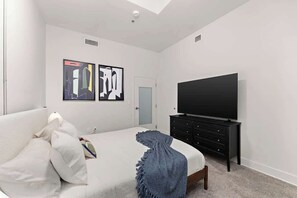 Une chambre à coucher comprenant un lit, une commode, un téléviseur et deux œuvres d’art murales.