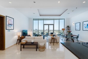 A spacious living area with a large window, a sofa, a coffee table, and a dining table with chairs.