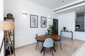 A modern dining area with a round wooden table, six chairs, and a vase of flowers. There are framed artworks on the wall and a floor lamp.