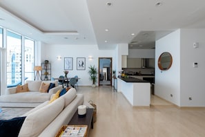 A modern living room with a sofa, a coffee table, and a dining area with a table and chairs. There is a kitchen area with a counter and cabinets.