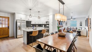 Une cuisine moderne dotée d’un îlot central, d’appareils électroménagers en acier inoxydable et de luminaires suspendus.