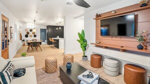 Un salon moderne doté d’un téléviseur à écran plat, d’un ventilateur de plafond et d’un coin repas avec une table et des chaises.
