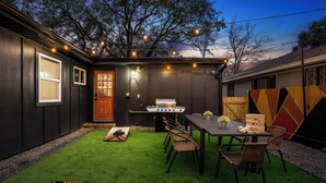 Un jardin avec un barbecue, une table à manger avec des chaises et un petit espace de jeux.