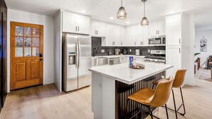 Une cuisine moderne avec des armoires blanches, des appareils en acier inoxydable et un îlot central doté de tabourets de bar.