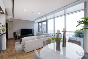 A modern living room with a large window, a flat-screen TV, a sofa, and a dining table.