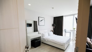 Ein modernes Hotelzimmer mit Bett, Schreibtisch, Stuhl, kleinem Tisch und einem Fenster mit Vorhängen.