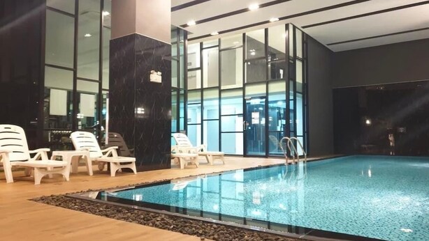 Ein beheiztes Hallenbad mit klarem Wasser, umgeben von Liegestühlen und einer Holzterrasse.