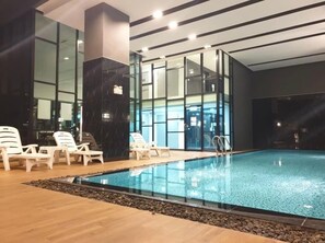 An indoor swimming pool with clear water, surrounded by lounge chairs and a wooden deck.