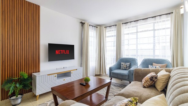 A living room with a TV mounted on the wall displaying 'NETFLIX', a sofa, a coffee table, and a potted plant. - Spacious 3-bedroom apartment with WiFi, swimming pool in vibrant Tatu City (Tatu City)