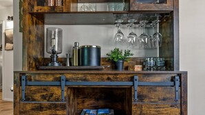 Un meuble en bois rustique, doté d’étagères, d’un porte-bouteilles et d’une petite plante.