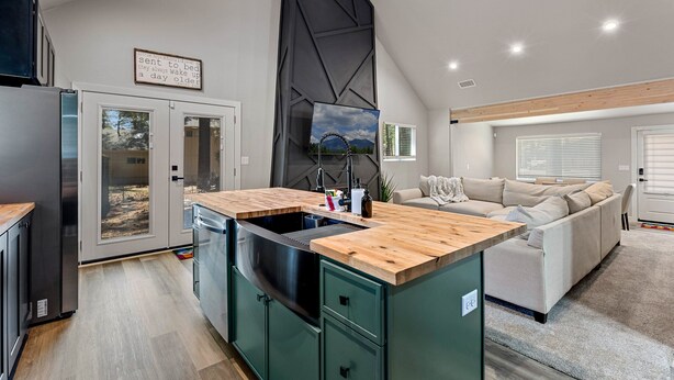 A modern kitchen with a wooden countertop and green cabinets, a built-in sink, and a dining area with a wooden table. - Pine Del | 3BR/2BA | Spend Spring in Flagstaff! (Flagstaff)