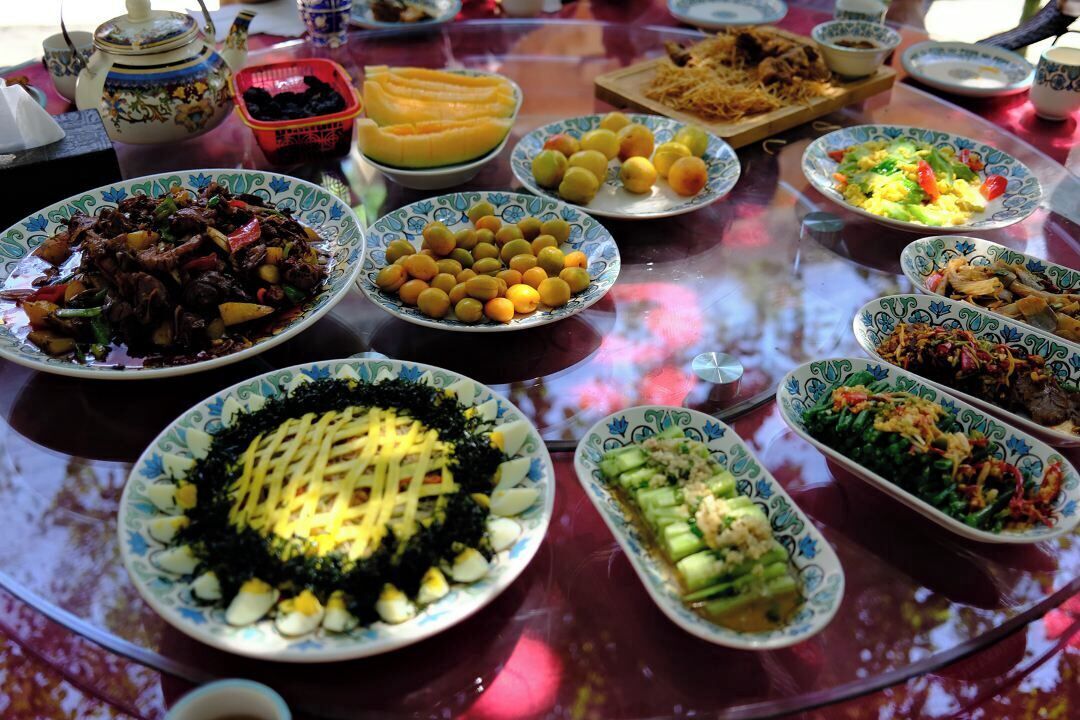 Una mesa con varios platos, incluyendo un plato con carne, un plato con frutas amarillas y un plato con verduras verdes.