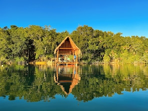 Une cabane à toit de chaume offrant une vue sur un lac paisible et une végétation luxuriante.