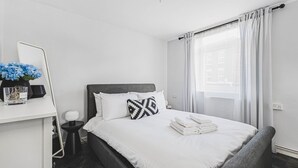 Quarto de hotel com cama, mesa de cabeceira, espelho e janela com cortinas.