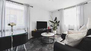 Uma sala de estar moderna com uma mesa de vidro, sofá preto e uma TV em um suporte preto.