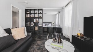 Uma sala de estar moderna com um sofá preto, uma mesa de centro de vidro e um painel de TV preto.