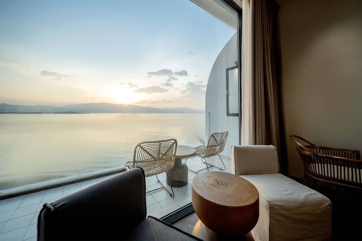Un balcon avec vue sur la mer, des fauteuils en osier, une table en bois et un canapé.