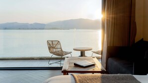 Une chambre avec vue sur un lac, un lit, une table avec un livre et deux chaises.