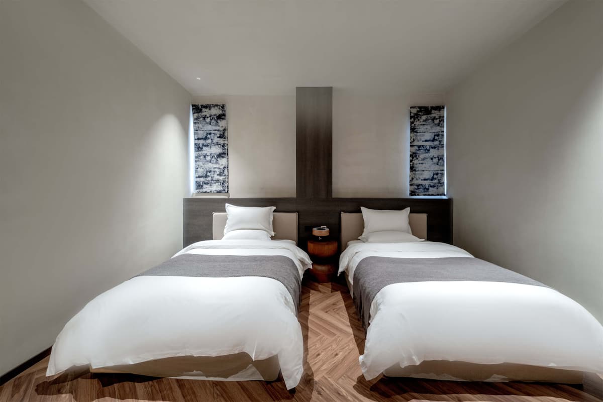 Une chambre d’hôtel moderne avec deux lits simples, un plancher en bois et une grande fenêtre donnant sur un beau paysage.