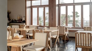 Un restaurant avec des tables et des chaises en bois, de grandes fenêtres donnant sur l’extérieur.