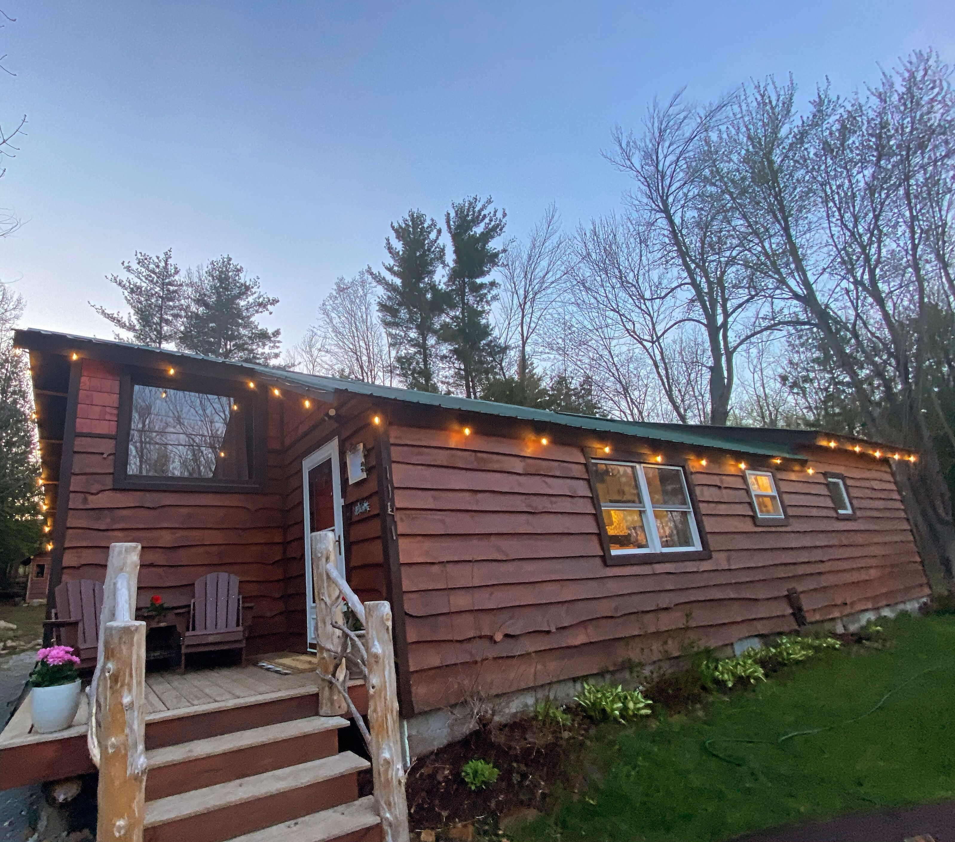 Une cabane rustique avec une façade en bois, une véranda dotée de chaises en bois et illuminée de guirlandes lumineuses.