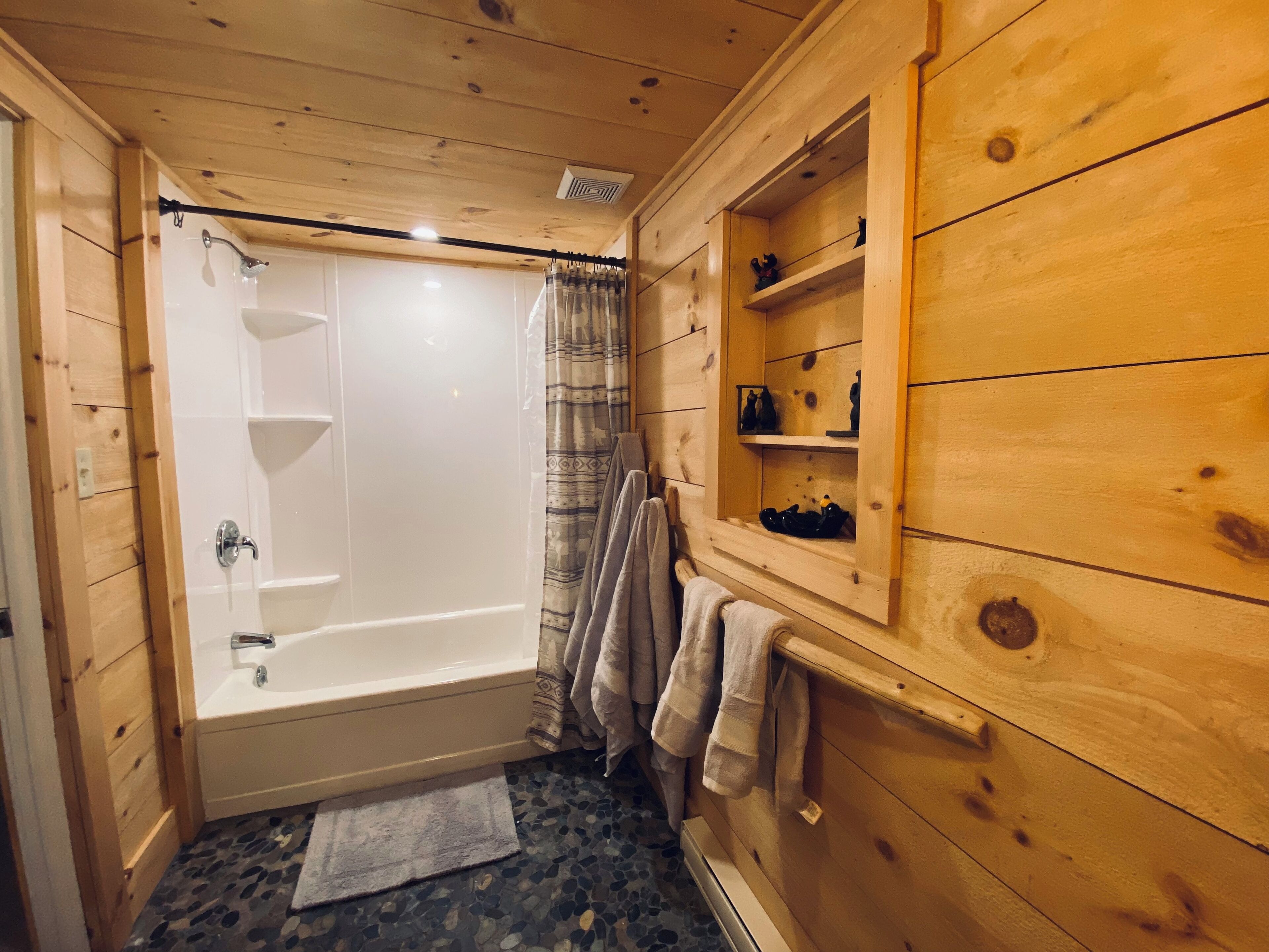 Une salle de bain rustique, aménagée dans une cabane en bois, avec une baignoire, une douche et des étagères où sont rangés les produits de toilette.