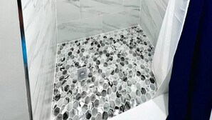 Una ducha con pared de mármol y suelo de baldosas hexagonales.