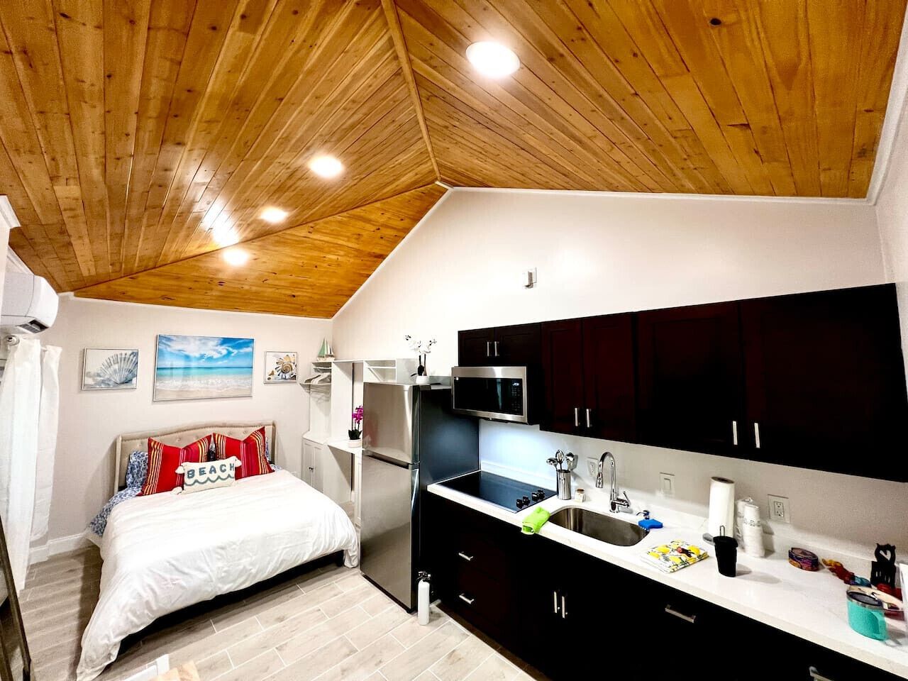 Una habitación compacta con cama, una kitchenette pequeña y techo de madera.