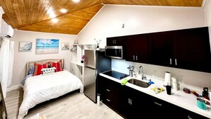 Una habitación compacta con cama, una kitchenette pequeña y techo de madera.