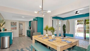 A modern kitchen with teal cabinetry, a stainless steel refrigerator, and a dining area with a wooden table and benches.