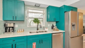 A modern kitchen with teal cabinets, stainless steel appliances, and a window with a plant.