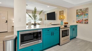 A modern kitchen with teal cabinetry, stainless steel appliances, and a flat-screen TV mounted on the wall.