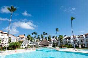 A resort with a swimming pool, palm trees, and white buildings with red roofs. - Apartment with pool views and private beach area. (Punta Cana)