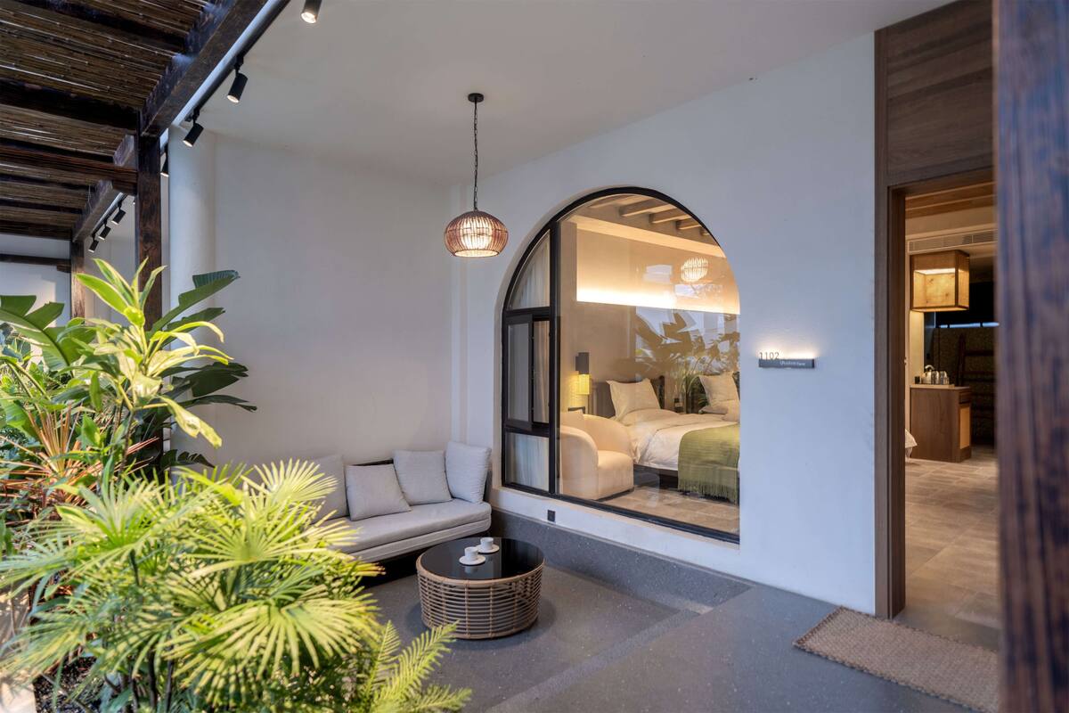 A modern interior with a large arched window, a sofa, a round table, and a hanging light fixture.