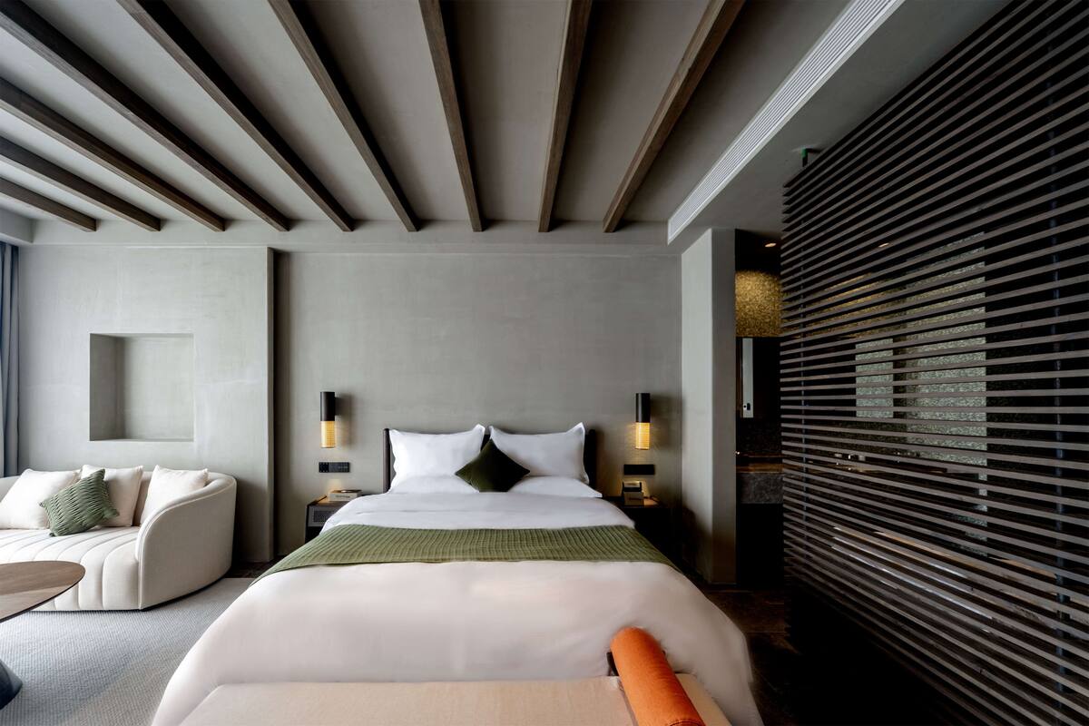 A modern hotel room with a large bed, a sofa, and a nightstand with two wall-mounted lamps.