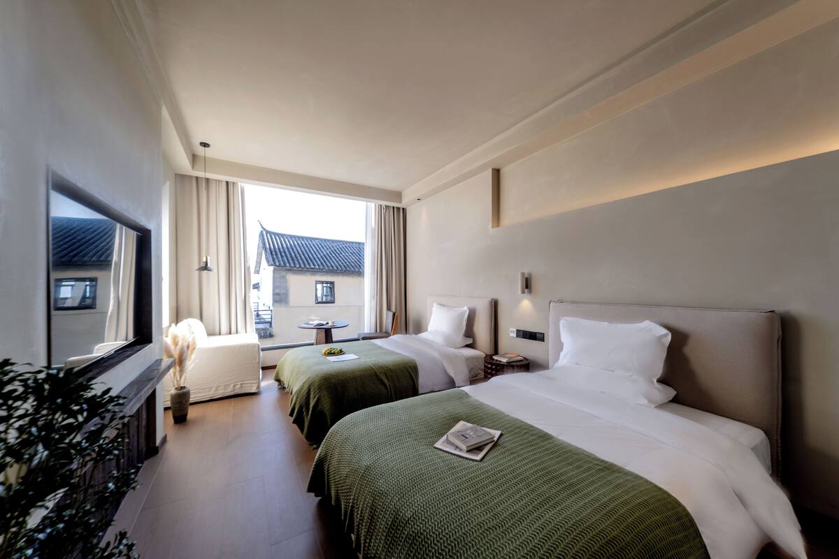 A hotel room with two beds, a sitting area, and a view of the outside.