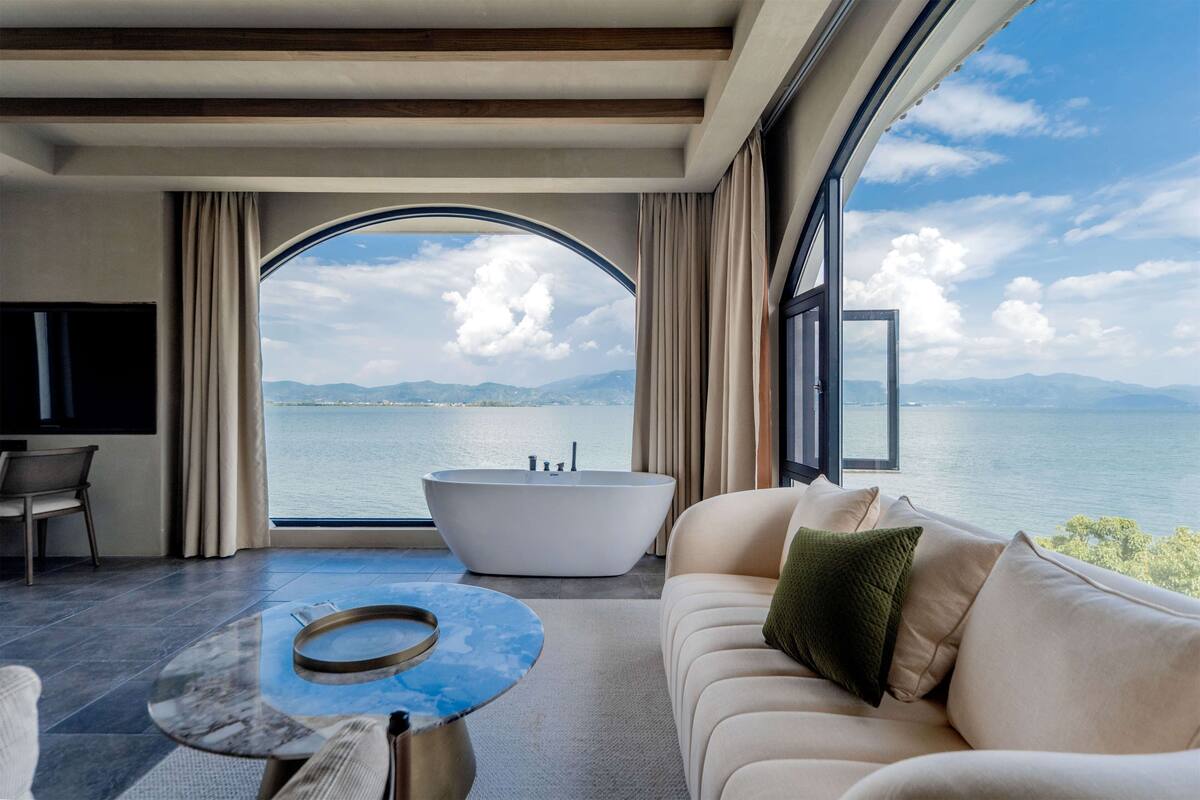 A modern room with a large window, a bathtub, a sofa, and a coffee table.