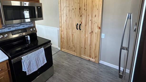 A kitchen with a stainless steel microwave, oven, and refrigerator, wooden cabinets, and a sliding wooden door closet. - 3-bedroom house in charming Green Bay, walking distance to LAMBEAU!! (Green Bay)