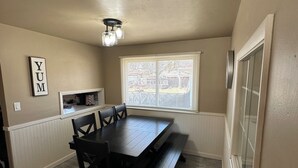 A dining area with a dark wooden table and chairs, a bench, a ceiling light fixture, a window with blinds, and a wall-mounted phone. - 3-bedroom house in charming Green Bay, walking distance to LAMBEAU!! (Green Bay)
