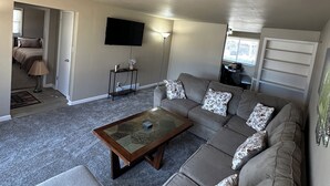 A living room with a sectional sofa, a glass coffee table, a flat-screen TV mounted on the wall, and a lamp. - 3-bedroom house in charming Green Bay, walking distance to LAMBEAU!! (Green Bay)