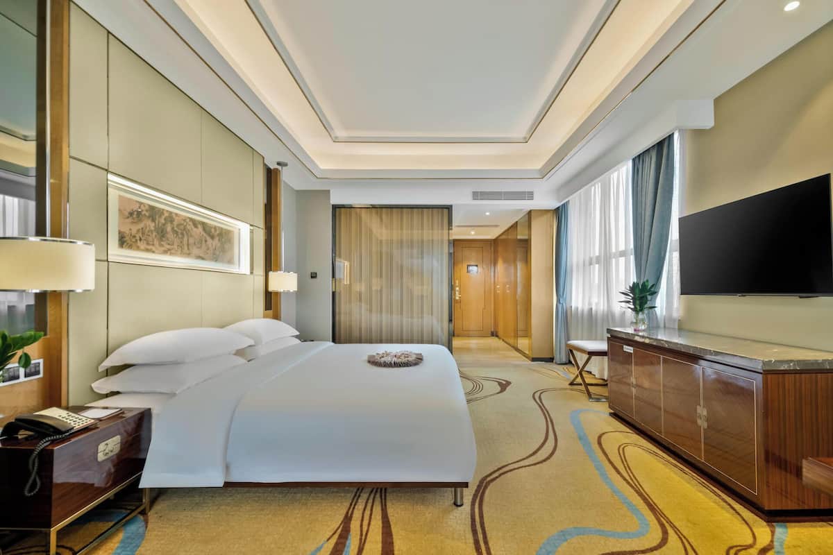 A hotel room with a large bed, a desk with a telephone, a TV, and a cabinet.